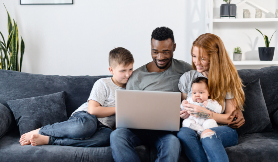 A family sits on a couch and looks at a laptop computer