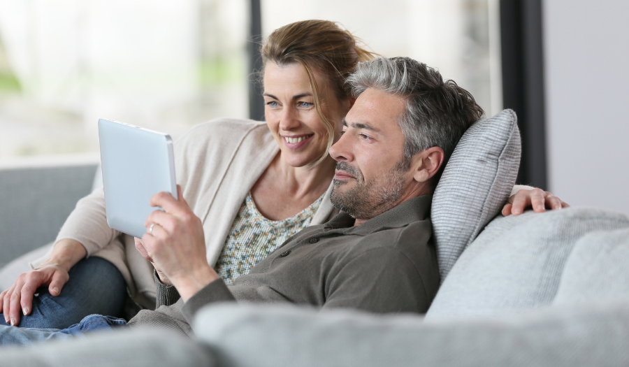 A man and a woman sit on a couch together and look at the screen of a laptop.